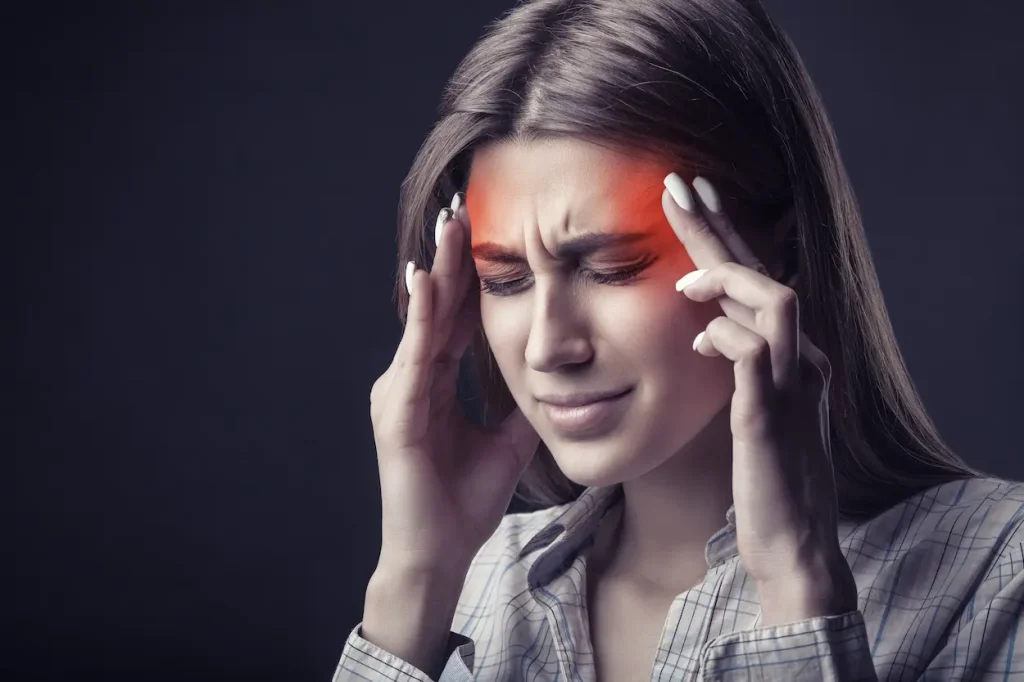 a woman with a migraine, surrounded by health items like medication and a heating pad.