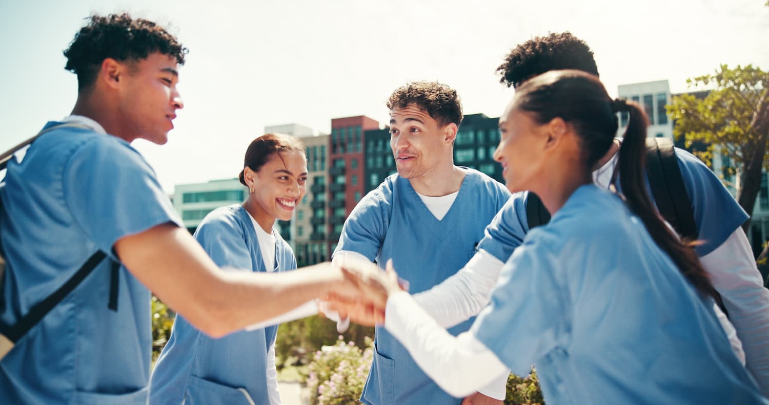 A group of healthcare professionals in scrubs shaking hands, symbolizing collaboration in Alzheimer's Disease care.