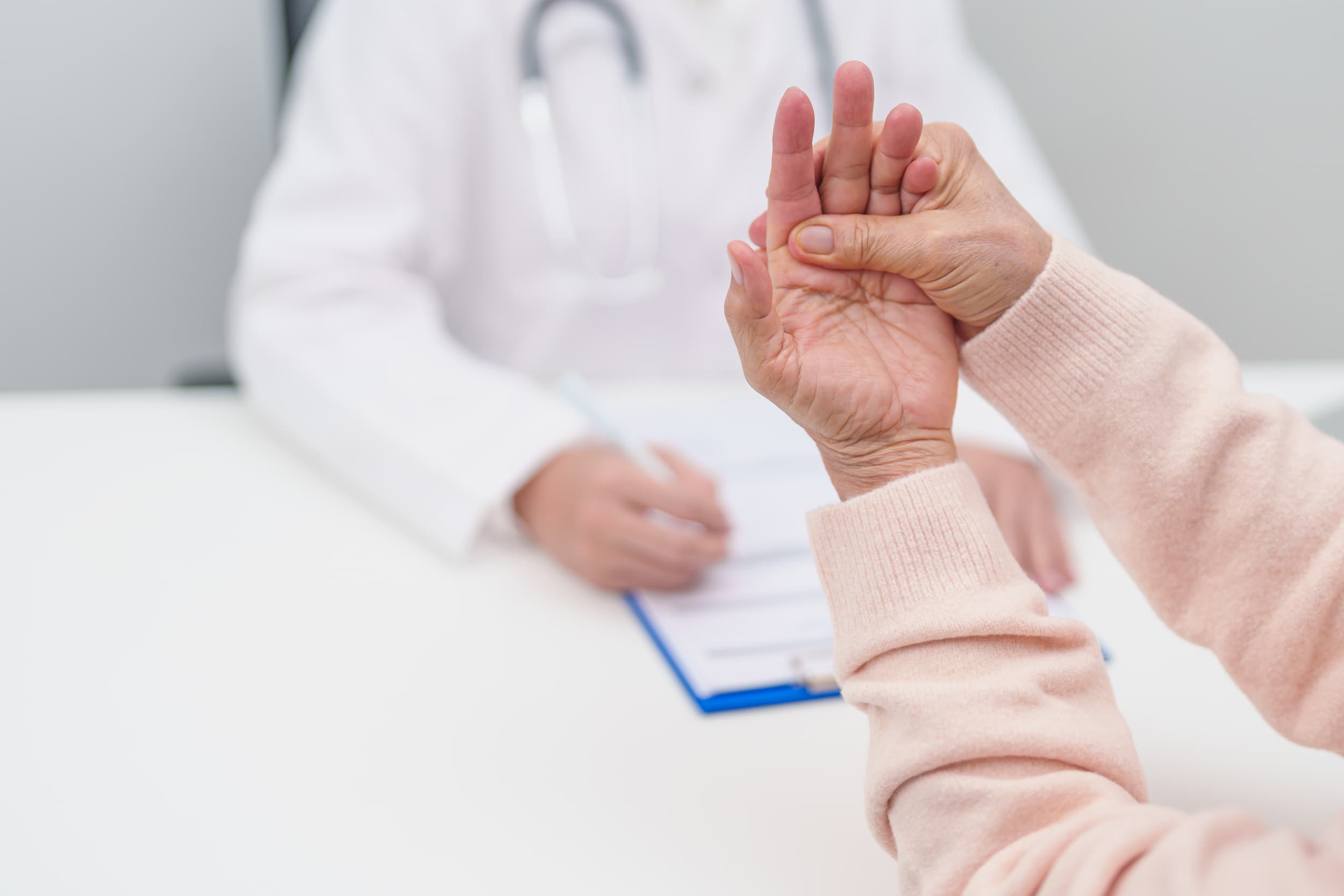 A woman raises her hand to a doctor, discussing her symptoms related to Parkinson’s Disease.