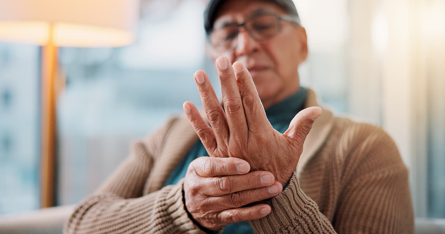 A man with arthritis and Parkinson’s Disease holds his hand to his face, expressing discomfort or contemplation.